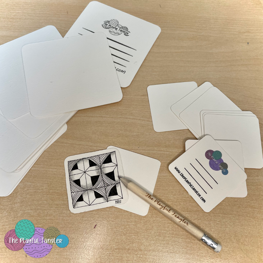 Picture of Zentangle resource pack (tiles only) on a desk with an example Zentangle picture.  Pack contains 10 original square tiles, 10 mini tiles and a Playful Tangler Pencil. 